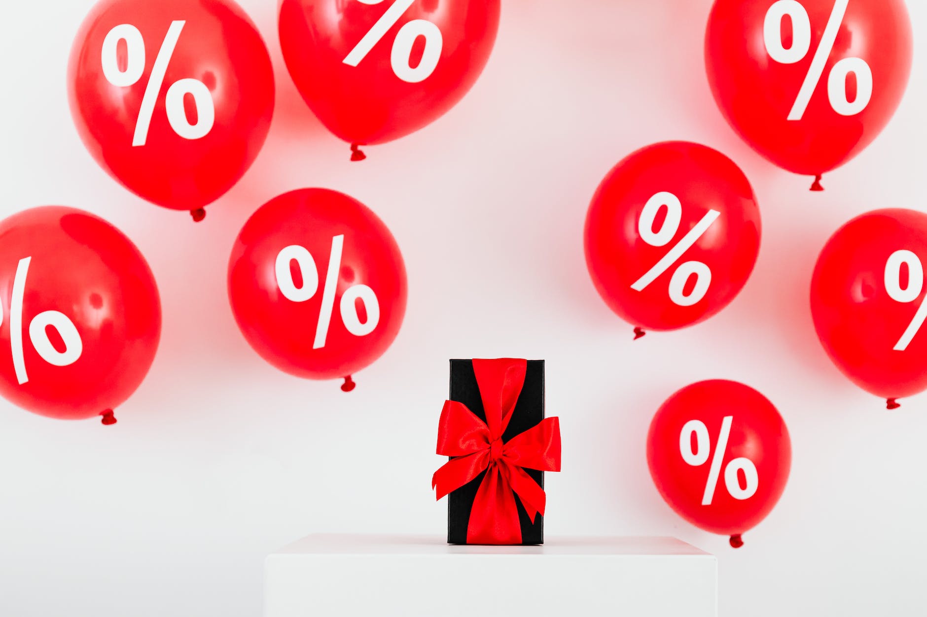 a gift with red ribbon in between red balloons with percentage symbols on a white background